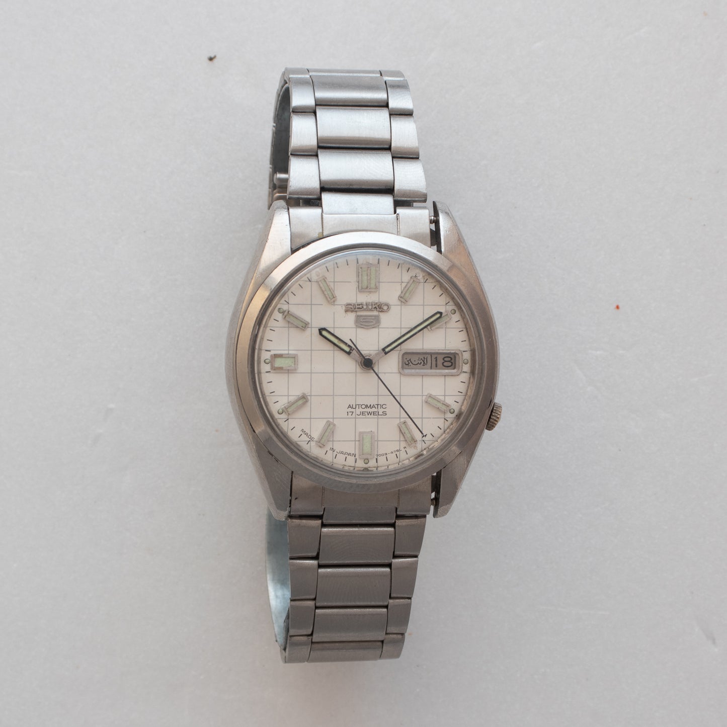 Silver wristwatch with a white face on a light gray background